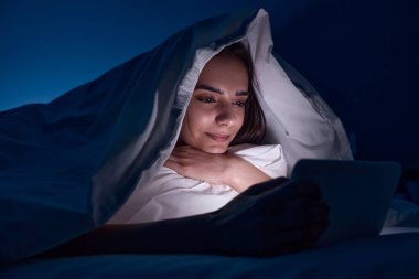 Gece yatakta film izleyen bir kadın.