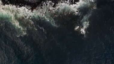 Taş plajı ve dalgalar büyük volkanik kayaların üzerine düşüyor.