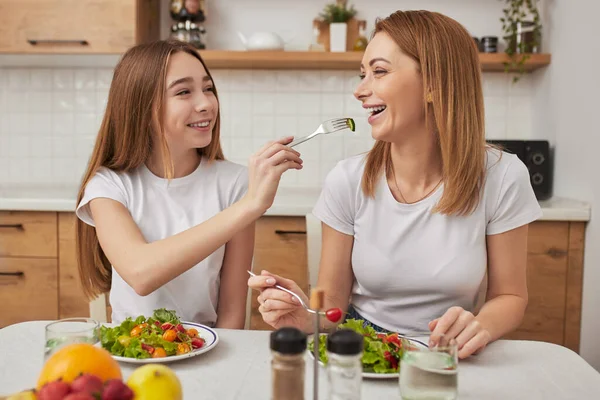 Sonriente hija alimentando alegre madre con ensalada — Foto de Stock