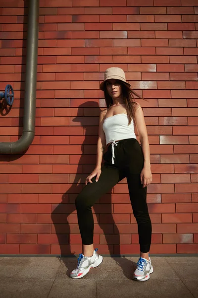 Stylish woman in hat standing near brick wall — Stock Photo, Image