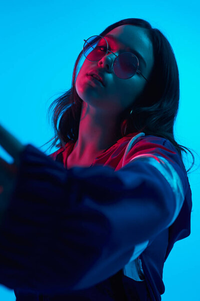 Trendy woman in sunglasses standing in neon illumination