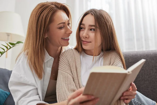 Glückliche Mutter und Tochter schauen einander beim Lesen von Büchern auf dem Sofa an — Stockfoto
