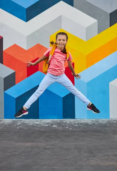 Весела школярка стрибає біля стіни графіті — стокове фото