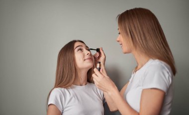 Gülümseyen genç anne kızına makyaj yapıyor.