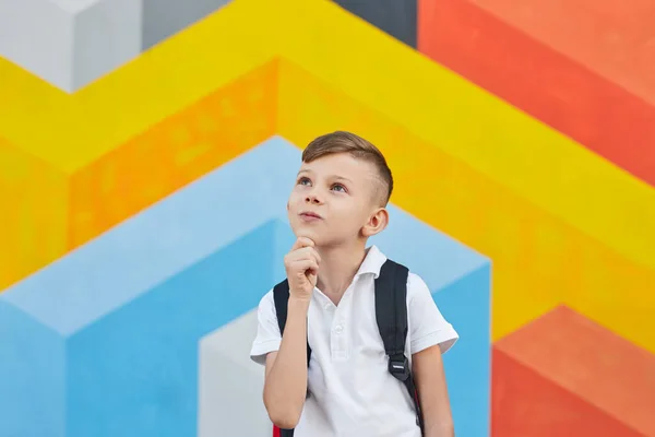 Bedachtzame schooljongen kijkt op tegen kleurrijke muur — Stockfoto