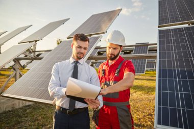 Girişimci, güneş enerjisi santralinde müteahhitle gazete okuyor.
