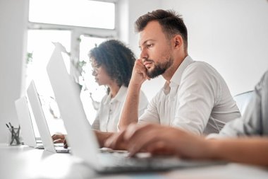 Ofiste dizüstü bilgisayarda çalışan düşünceli bir adam.