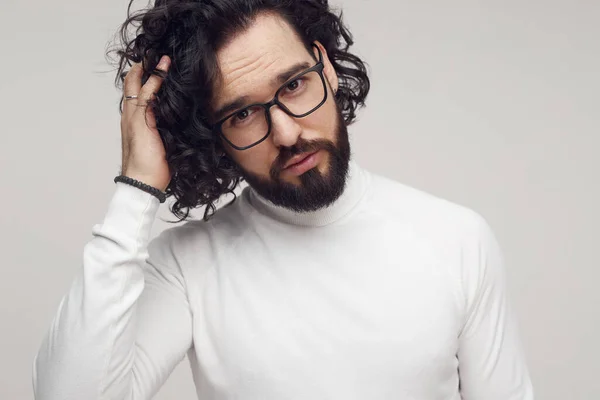 Jistý vousatý muž v brýlích dotýkající se vlasů ve studiu — Stock fotografie