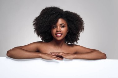 Gri arka plan karşıtı reklam kampanyası sırasında çıplak omuzlu, kıvırcık saçlı, boş beyaz posterli, pozitif Afro-Amerikan kadın modeli.