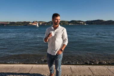 Zeki, sıradan giysiler içinde, cebinde kahveyle gezen bir adam, yaz günü setin kenarındaki su taşının üzerinde dikilmiş, kafasını çevirmeye çalışıyor.