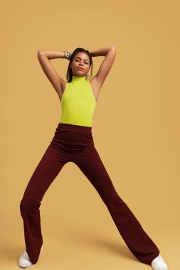 Kendine güvenen, modaya uygun, şık giyimli, uzun siyah saçlara dokunan ve stüdyoda sarı arka planda dururken kameraya bakan genç İspanyol modeller.