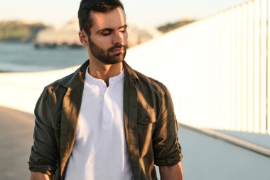 Yaz günü şehirde parlak güneş ışığı altında dikilirken koyu renk saçlı, yakışıklı genç adam gözlerini kapatıyor.