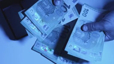 Unrecognizable criminal man counting counterfeit money under UV light. Checking euro banknotes in ultraviolet black light.