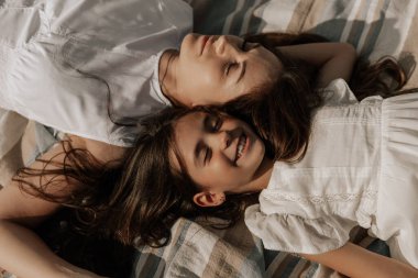 Barışçıl genç bir kadın ve uzun siyah saçlı, beyaz elbiseli mutlu bir kız gün batımında piknik yaparken gözleri kapalı battaniyede dinleniyor.