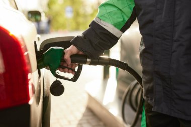 Crop anonymous male employee in protective uniform pouring fuel into tank of modern car while working in gas station on sunny day