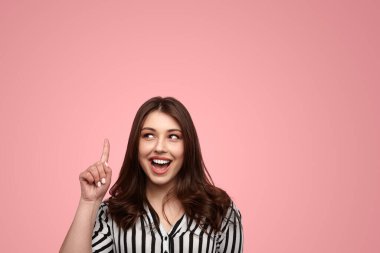 Zeki, pozitif, genç bir kadın artı uzun siyah saçlı, günlük kıyafetlerle neşeli bir şekilde gülümseyen ve pembe arka plana bakan bir model.