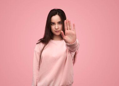 Uzun siyah tişörtlü, kendine güvenen genç bir manken. Dur hareketi yapıyor ve pembe arka planda kameraya bakıyor.