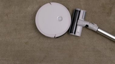 Vacuum Robot auto cleaning and classical vacuum cleaner lying down together at home on carpet. Comparison and competition between generations in housekeeping technology