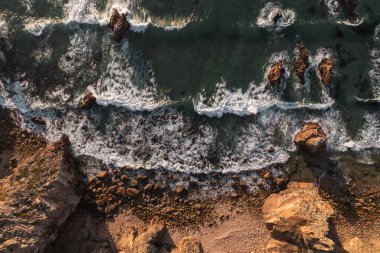 From above aerial view of foamy sea waves splashing near rocks on Ursa Beach on stormy day in Portugal