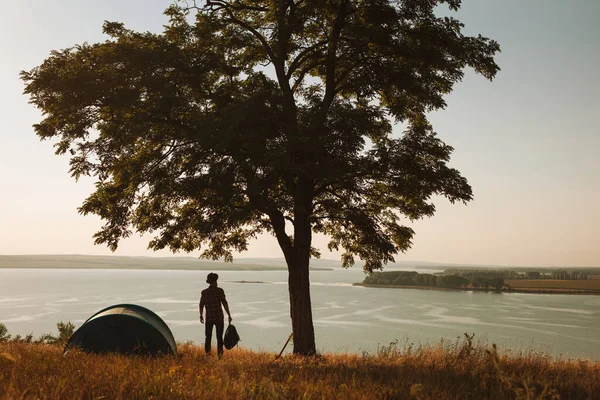 Silhouette Man Backpack Standing Tree Tent Admiring Lake Evening Campsite — Stok Foto