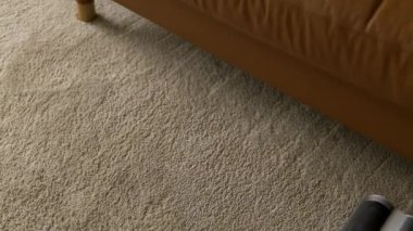 Rug dry cleaning with vacuum cleaner. Overhead shot of minimalist interior vacuuming carpet floor under sofa