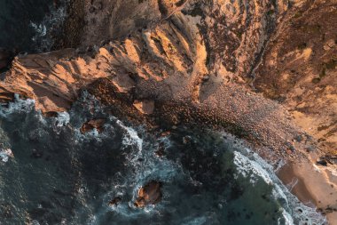 From above drone view of foamy sea waves splashing near rough rock formation in nature