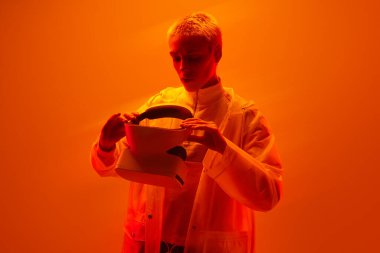 Siber uzayı keşfetmek için modern VR kulaklığı takan kısa saçlı, turuncu neon ışıkla stüdyoda duran ciddi bir kadın.