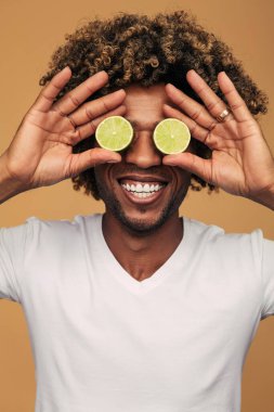 Beyaz tişörtlü, kıvırcık saçlı, neşeli Afro-Amerikan bir adam. Kahverengi arka planda taze kireç parçaları tutuyor.