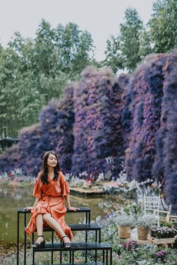 Ormanın ortasında kahverengi bir elbise giymiş güzel bir kadın. Renkli çiçeklerle dolu, güzel bir kadın. Çiçek bahçesini geziyor, rahatlamak ve mutlu bir tatil için fotoğraf çekiyor..