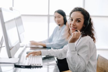 Sekreter operatörü danışman yardımı için bir kulaklık ve mikrofon takar, çağrı merkezi personeli kameraya bakarken gülümseyen ve mutlu bir şekilde müşterilere tavsiye ve yardım eder