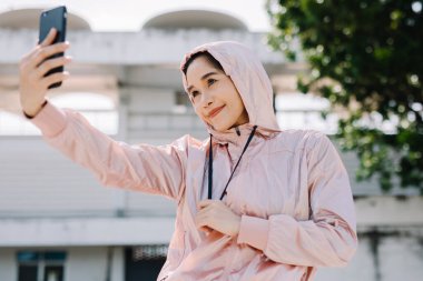Spor salonundaki güzel bir kadın akıllı telefonuyla ayakta duruyor ve gün boyunca binanın dışındaki ekrana bakıyor. iletişim konsepti