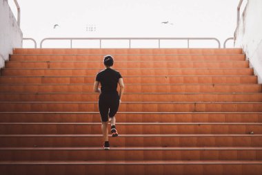 Güzel bir kadın koşucu gün ışığının altında merdivenleri tırmanıyor. Başarı kavramı, egzersizdeki kendini geliştirme..