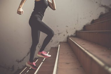 Güzel bir kadın koşucu gün ışığının altında merdivenleri tırmanıyor. Başarı kavramı, egzersizdeki kendini geliştirme..