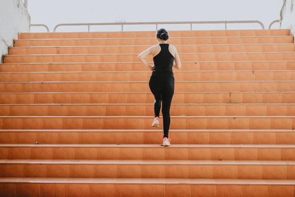A beautiful woman runner is jogging up the steps under the sunlight. The concept of stepping into success, self-improvement in exercise.