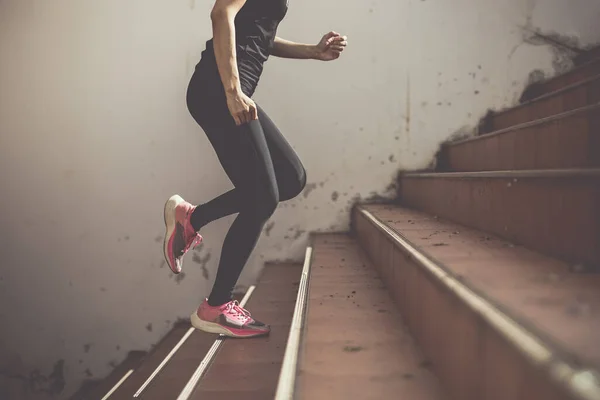 A beautiful woman runner is jogging up the steps under the sunlight. The concept of stepping into success, self-improvement in exercise.