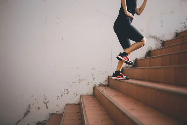 A beautiful woman runner is jogging up the steps under the sunlight. The concept of stepping into success, self-improvement in exercise.