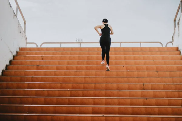 A beautiful woman runner is jogging up the steps under the sunlight. The concept of stepping into success, self-improvement in exercise.