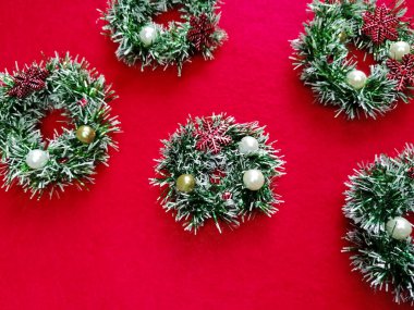 Kırmızı arka planda, yeşil süs ve renkli boncuklardan oluşan çelenkler. Kar taneleri.