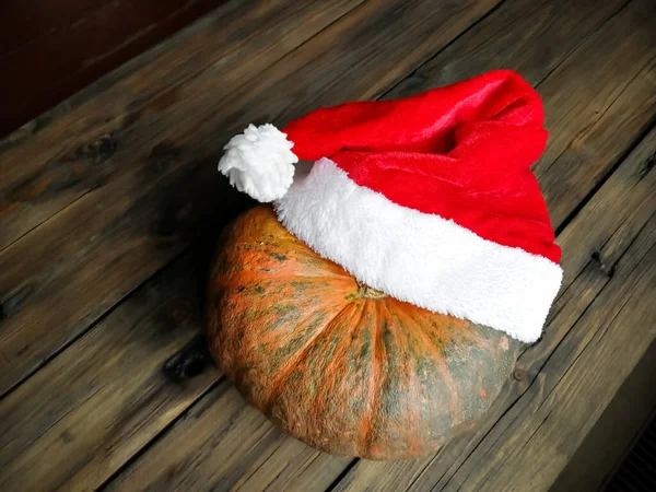 Pumpa på ett träbord i en nyårshatt. Jultomten jul hatt på en grönsak. — Stockfoto