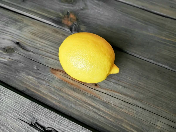 A ripe, yellow lemon lies on a wooden table. — Stock Photo, Image
