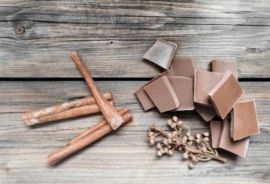 Tahta bir masanın üzerinde çikolata, tarçın çubukları ve defne tohumları var. Kahverengi ve gri ahşap arka plan. Baharatlar ve çikolata. Baharatlı sütlü çikolata..
