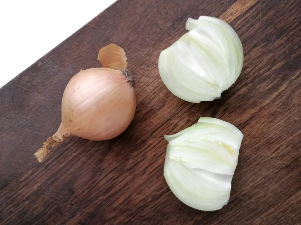 En la tabla de cortar se encuentra una cebolla entera y otra cebolla cortada en dos mitades. Cebollas en una tabla de jereview. — Foto de Stock