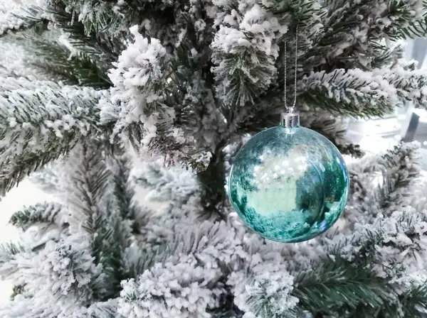 Una bola de vidrio azul en un árbol de Navidad cubierto de nieve. árbol de Navidad artificial. Árbol de Navidad cubierto de nieve. — Foto de Stock