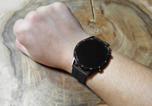 Relógio inteligente preto em uma mão de homem. Fundo de madeira. Novo relógio inteligente na mão de um homem. Mão bronzeada, preta. — Fotografia de Stock