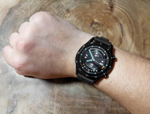 Une montre intelligente noire sur une main d'homme. Fond en bois. Nouvelle montre intelligente sur la main d'un homme. Main bronzée, noire. — Photo