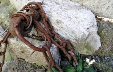 Eski, paslı bir zincir duvara tutturulmuş. Eski harabeler. Zincir takmak suçtur. Paslı metal