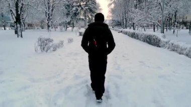 Bir adam karda yürür. Karanlık bir Ojezhd giymiş bir adam karda yürüyor. Arkasından manzara. Geri çekilen adamın arkası. kış.