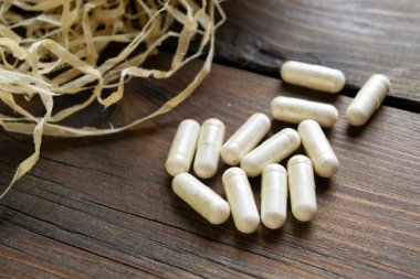 Ahşap arka plan kapsüllerinde otlar ve kuru otların yanında. Kuru ot ve katkı maddeleriyle dolu sağlıklı kapsüller. Kapsüllerdeki vitamin lifleri. Ahşap bir masada otlu şeffaf kapsüller..