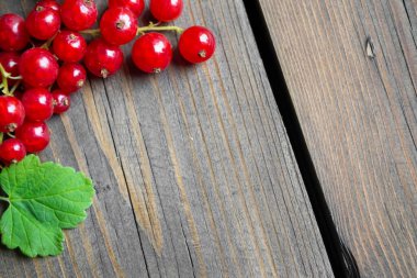 Ahşap bir masanın üzerinde yeşil yapraklı frenk üzümü var. Yazıtın altında yer var. Fotoğrafın köşesinde yapraklı kırmızı bir frenk üzümü var. Yazıtın altındaki fotoğraf.