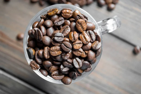 Bardakta kahve çekirdekleri, üst manzara. Kahve çekirdekli ahşap bir masada bir bardak. Bardaktaki tahıllar. Ahşap bir arka planda cam bir şişede bir sürü kahve çekirdeği..